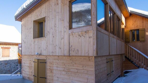 A wooden cabin with large windows, a covered porch, and a staircase leading to the entrance.