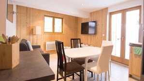 A modern dining area with a wooden interior, a flat-screen TV mounted on the wall, and a sliding glass door leading to the kitchen.