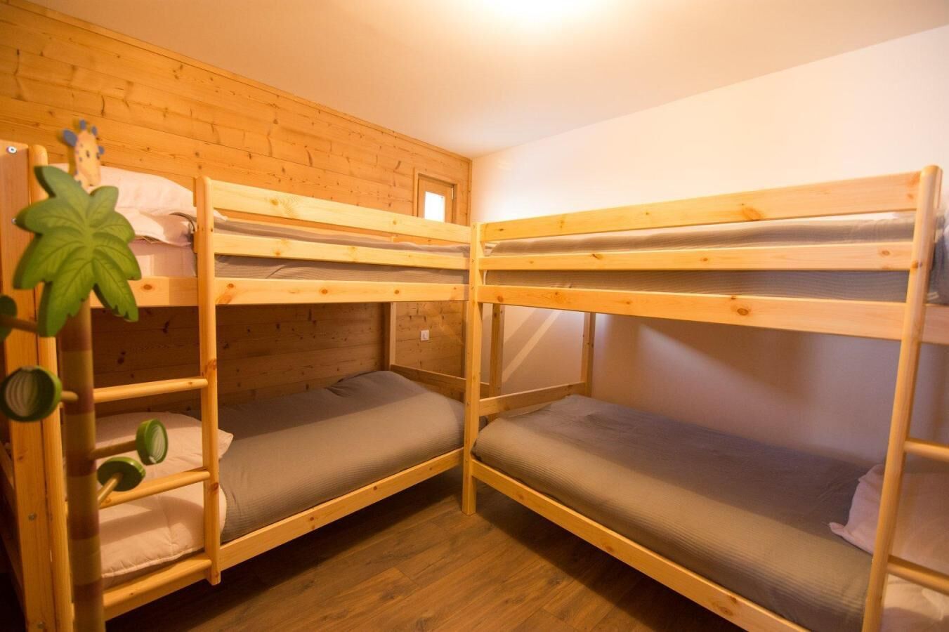 A room with two bunk beds, wooden walls, a small window, and a green plant.