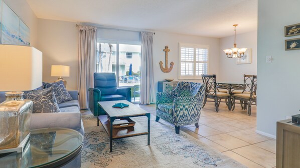 A living room with a sofa, armchair, coffee table, and dining area with chairs and a chandelier.