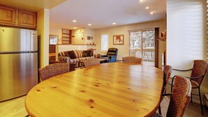 Un comedor amplio con una gran mesa de madera rodeada de sillas de mimbre, una cocina con un refrigerador de acero inoxidable y una sala de estar acogedora con sofá y chimenea.