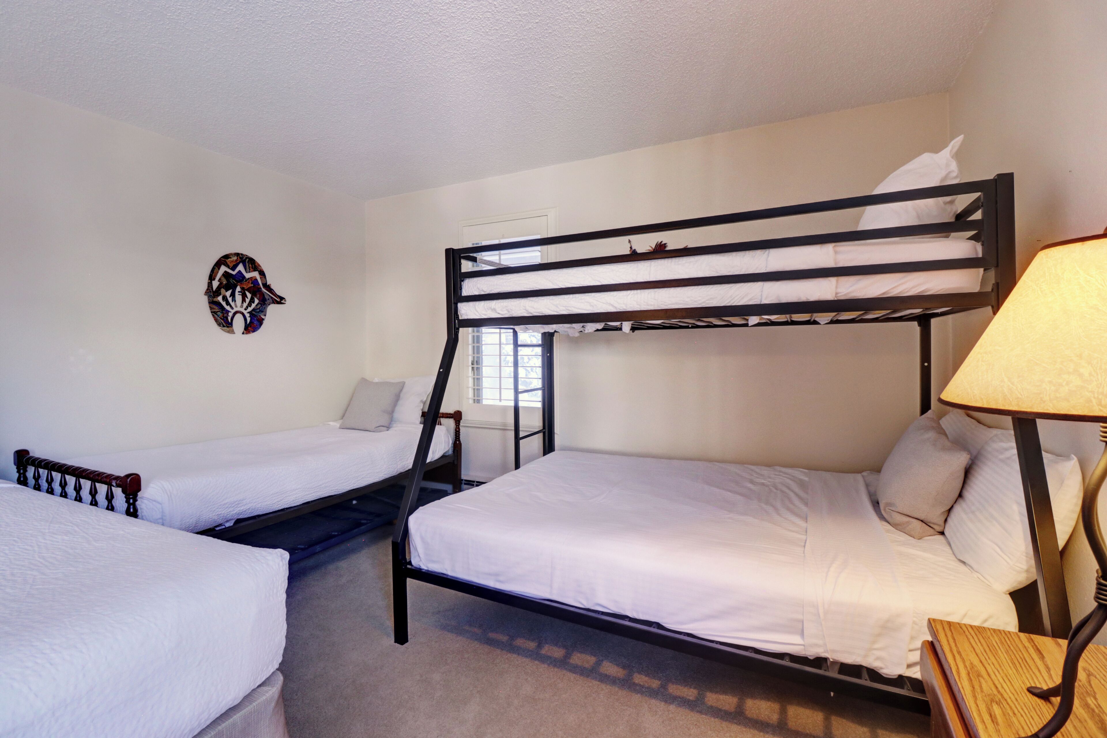 A room with two bunk beds, a wall-mounted headboard, a lamp, and a window.