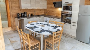 A modern kitchen with wooden walls, a round dining table set for four, and stainless steel appliances.