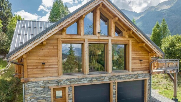 A modern log cabin with large windows, stone accents, and a garage.