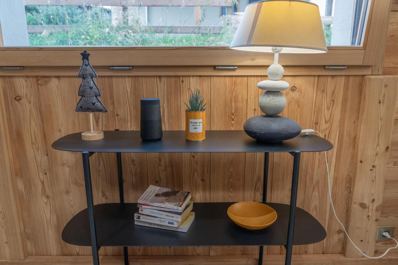A wooden table with a lamp, a small Christmas tree, a potted plant, and a stack of books.