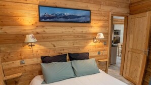 A wooden-paneled bedroom with a bed, pillows, two wall-mounted lamps, and a framed picture above the bed.