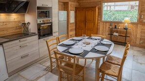 A modern kitchen with wooden paneling, a dining table set for four, and a large window providing natural light.