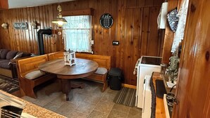 L’intérieur chaleureux d’un chalet comprend un coin repas en bois, une cuisine équipée d’une cuisinière et un espace détente avec un banc et un canapé.