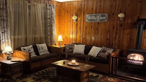 Un salon chaleureux avec un mur lambrissé, un ensemble de canapés, une table basse avec une bougie, un tapis et une cheminée.