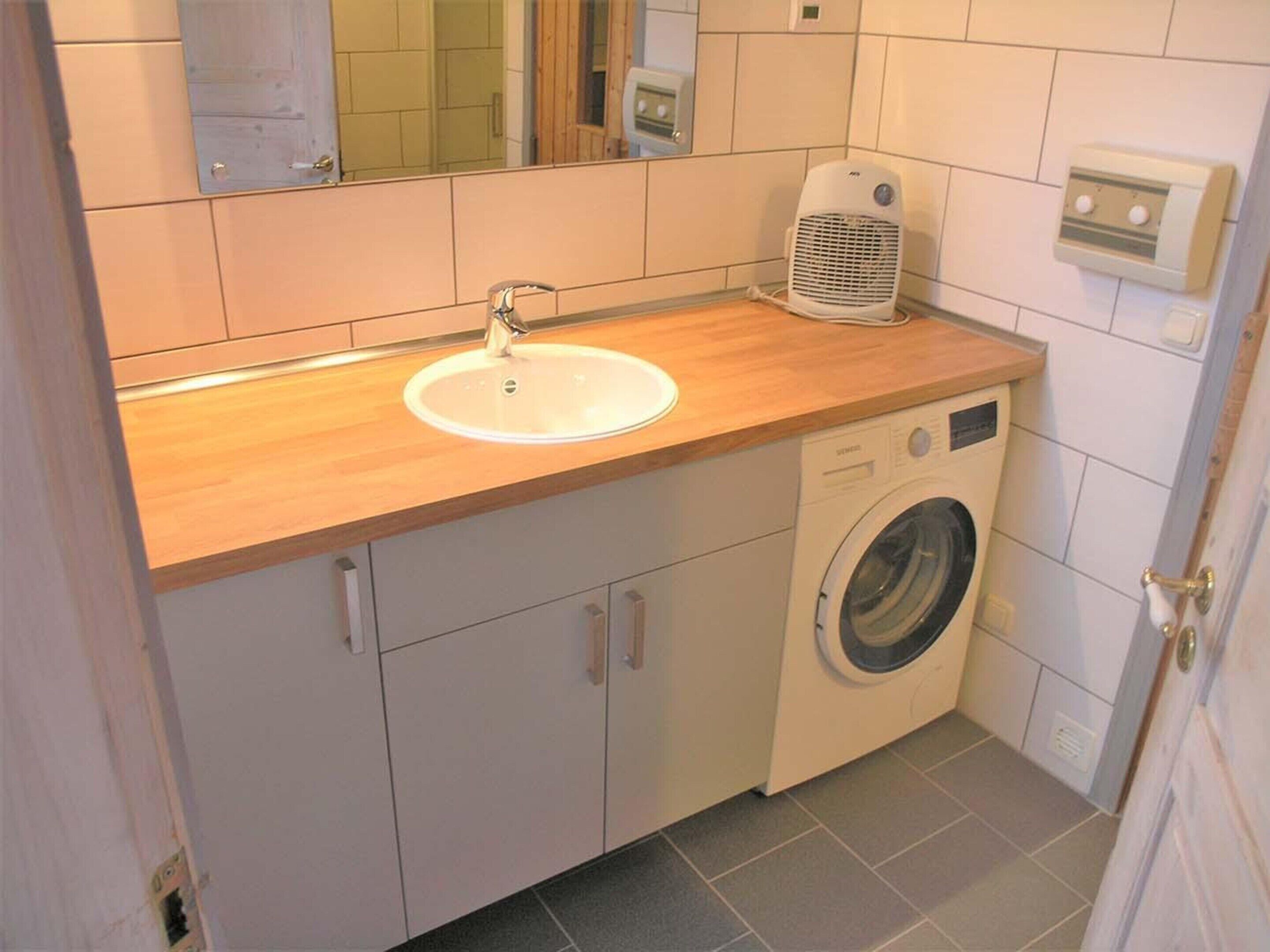 A compact bathroom with a sink, a washing machine, and a mirror.