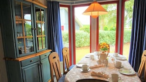 Un coin repas avec une table dressée pour quatre personnes, un meuble avec des portes en verre et une vue sur la verdure à l’extérieur.