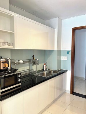 A modern kitchen with stainless steel appliances, white cabinets, and a black countertop. - Sky Center - Studio (Ho Chi Minh City)