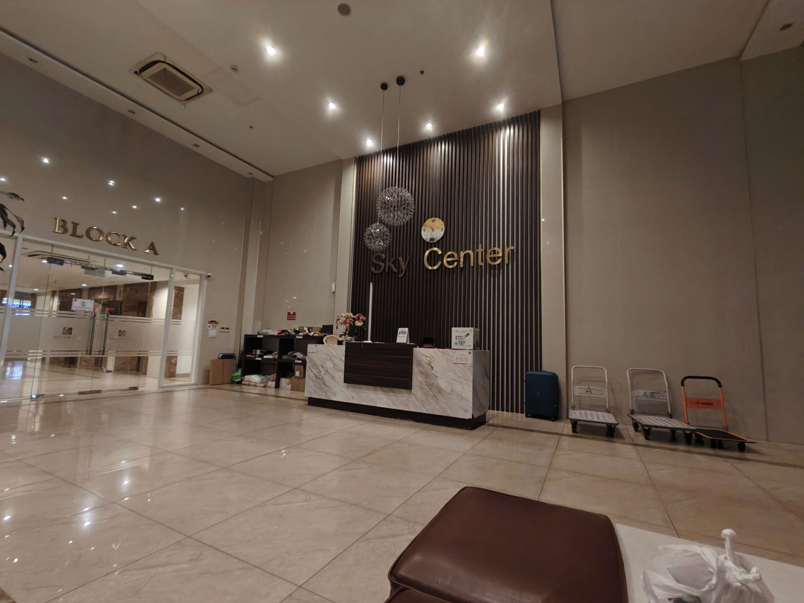 A hotel reception area with a reception desk, a clock, and a sign for 'Sky Center.'