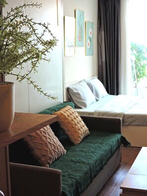A room with a bed, a green sofa, a wooden table, and a potted plant. - Sky Center - Studio (Ho Chi Minh City)