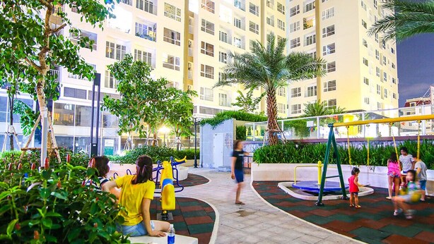 Un'area giochi con altalene e una struttura per arrampicarsi, immersa nel verde e con un edificio sullo sfondo.