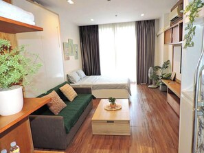 A compact living space with a sofa, a bed, a small table, and a potted plant. - Sky Center - Studio (Ho Chi Minh City)