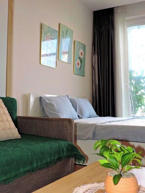 Une pièce avec un lit, un canapé vert et une petite table sur laquelle se trouve une plante. Trois tableaux sont accrochés au mur au-dessus du lit.