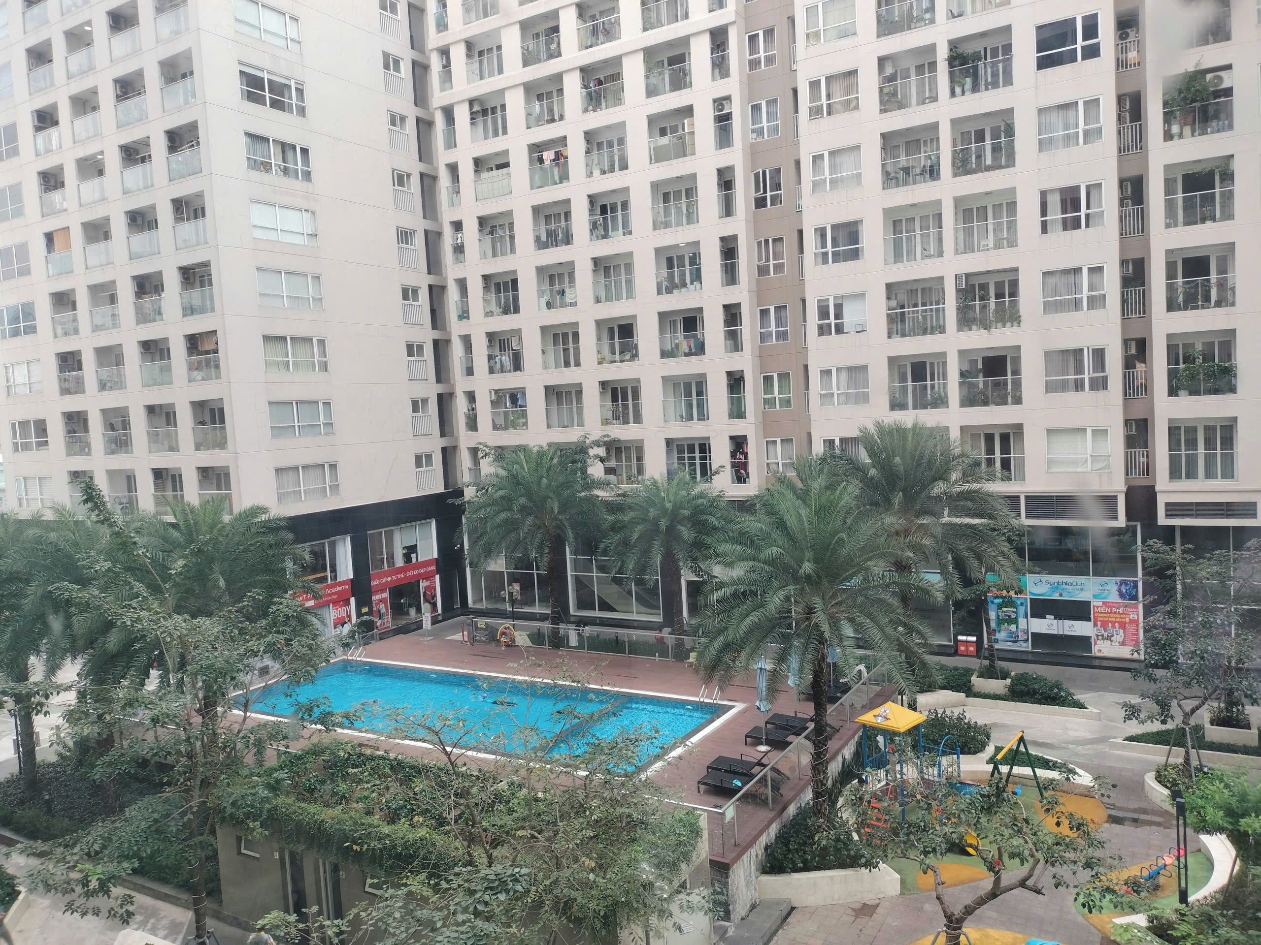 A high-rise residential building with multiple balconies, a swimming pool, and a playground.