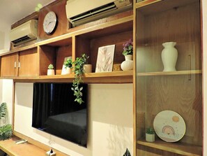 Une pièce dotée d’un téléviseur à écran plat fixé au mur, d’étagères en bois ornées d’objets décoratifs et d’un appareil de climatisation placé au-dessus du téléviseur.