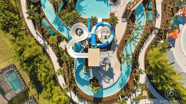 Vue aérienne d’un complexe hôtelier doté d’une piscine sinueuse, d’un toboggan aquatique et d’espaces de détente entourés de palmiers.