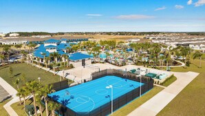 Vue aérienne d’un quartier résidentiel avec un grand terrain de basket-ball bleu, entouré de palmiers et bordé d’une piscine.