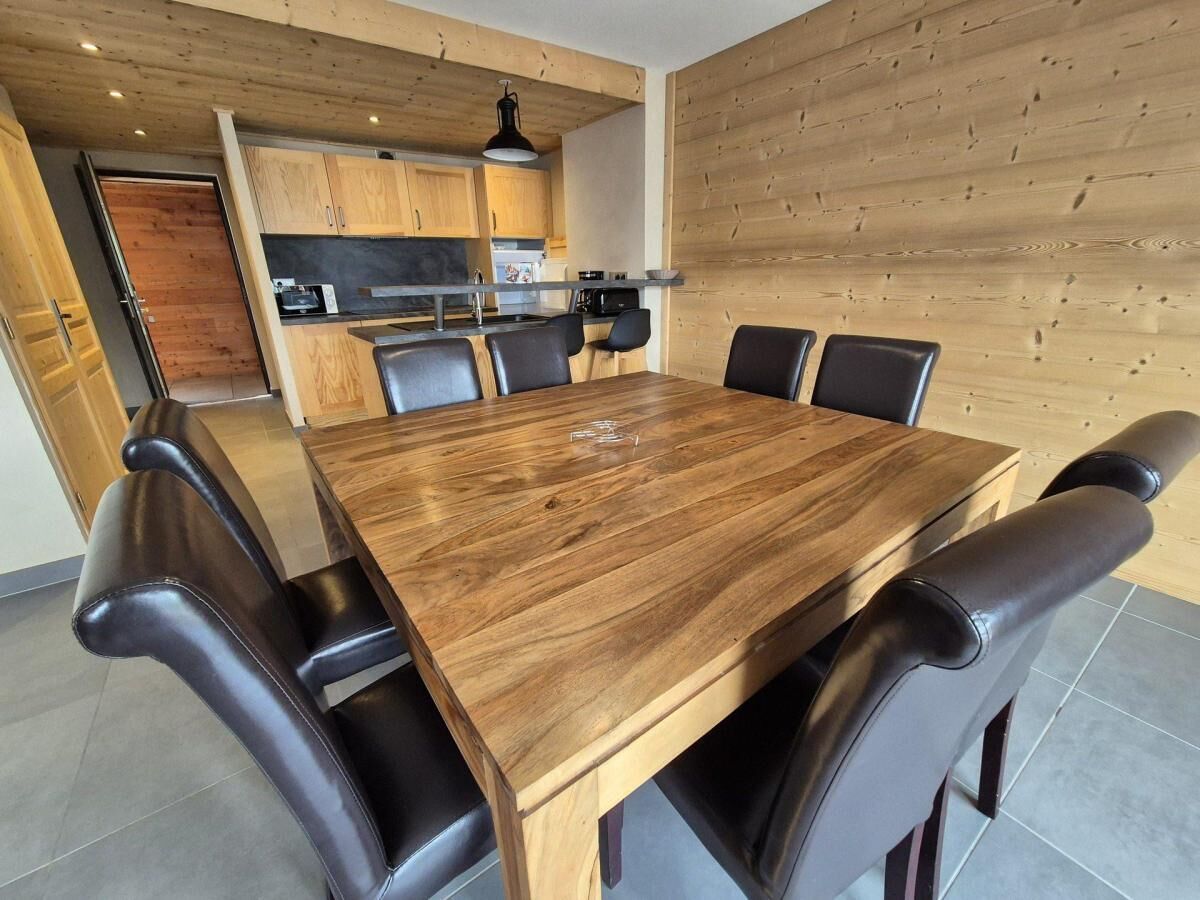 Ein Essbereich mit Holztisch und schwarzen Stühlen, im Hintergrund eine Küche und Holzwandverkleidung.