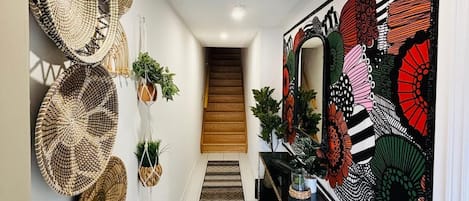 A hallway with a staircase, decorative woven baskets, a large abstract art piece, and a bench.