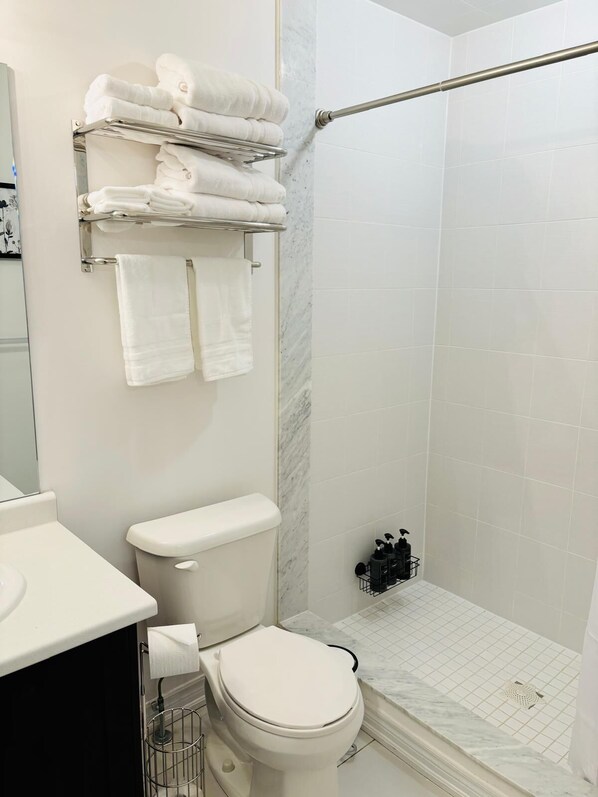 A bathroom with a toilet, a sink, a shower area, and a towel rack with folded towels. - Boho Chic Markham Family Stay, Special Summer Price!!! (Markham)