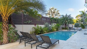 A swimming pool with lounge chairs, surrounded by palm trees and various plants. - Aruba Opal Rental I (Noord)