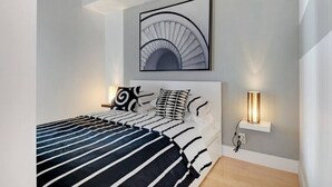 Un dormitorio moderno con una cama grande, cabecera, una obra de arte en la pared y lámparas de noche.