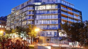 Un hotel de varios pisos con un diseño moderno, con balcones en cada planta y ventanas amplias.