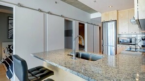 Una cocina moderna con encimera de granito, pileta de acero inoxidable y una puerta corrediza que da a otra habitación.