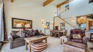 A cozy living room with a sofa, armchair, and ottoman, a dining table with chairs, and a staircase leading to an upper level. - Stunning Third Story Condo with Stunning Mountain Views (Keystone)