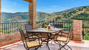 A terrace with a table set for dining, surrounded by brick pillars, offering a view of rolling hills and vineyards. - Casa Jorge in Frigiliana (Frigiliana)