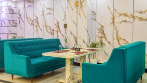 Un canapé et un fauteuil de couleur turquoise sont disposés autour d’une table à motifs de marbre, sur laquelle repose un centre de table en verre.