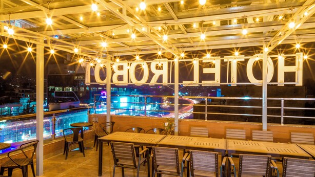 Un bar situé sur le toit, avec des tables et des chaises, une vue sur la piscine et des lettres lumineuses qui épellent le mot « HÔTEL ».