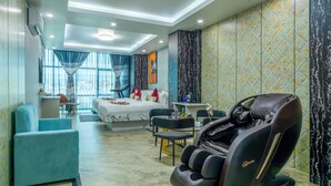 Une chambre d’hôtel moderne équipée d’un lit, d’un coin salon, d’un fauteuil massant et de grandes fenêtres.