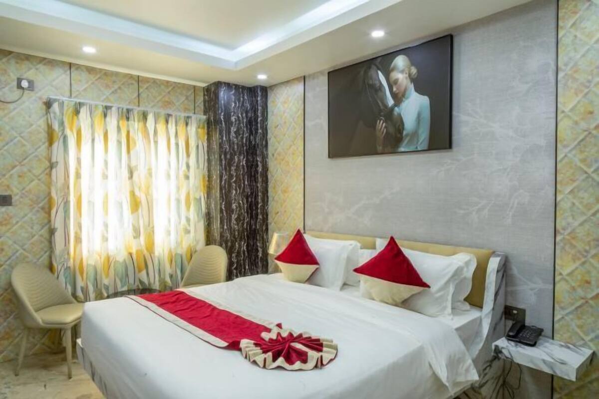 A hotel room with a bed, a chair, a curtain, a painting, and a telephone.