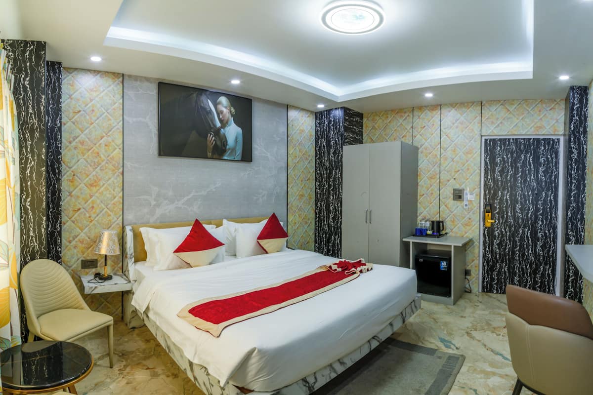 A hotel room with a bed, a desk, a chair, a wardrobe, and a painting on the wall.