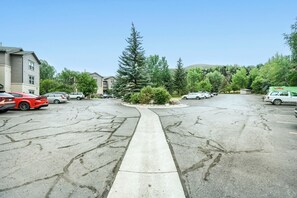 Un parking avec plusieurs voitures, une allée centrale et de la verdure tout autour.