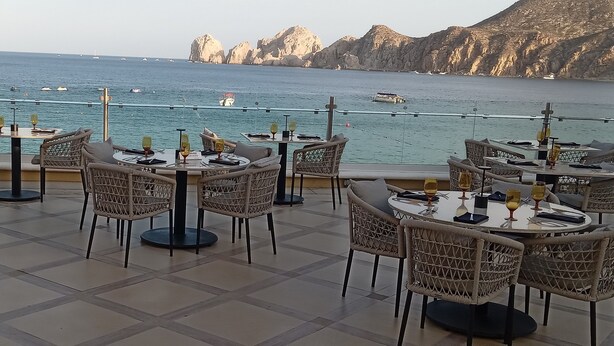 Une terrasse agrémentée de tables et de chaises, offrant une vue dégagée sur la mer, les bateaux et les falaises rocheuses.