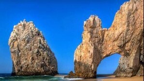 Une plage avec une eau d’un bleu limpide et une grande formation rocheuse.