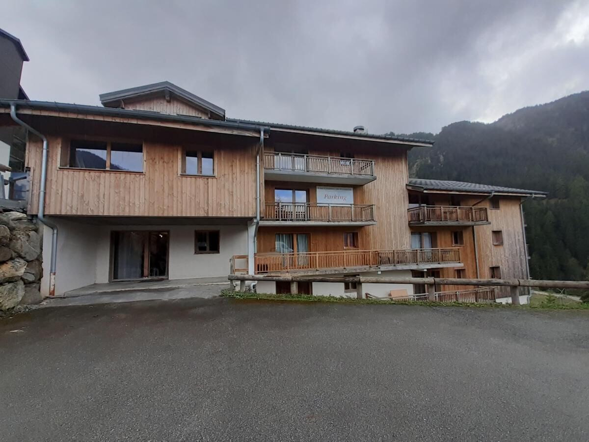 A two-story wooden building with a balcony on the upper floor, a sign indicating "Parking," and a stone wall to the left.