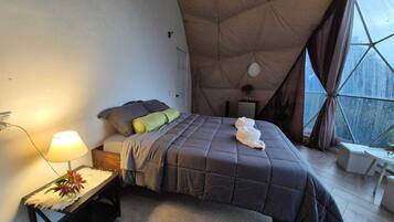 Une chambre confortable avec un lit, une table de chevet avec une lampe et une vue dégagée sur l’extérieur grâce à une grande fenêtre.