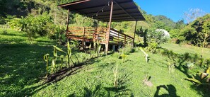 A rustic wooden structure with a metal roof, surrounded by lush greenery and a clear blue sky. - Glampling Nubes de Monteverde (Monteverde)