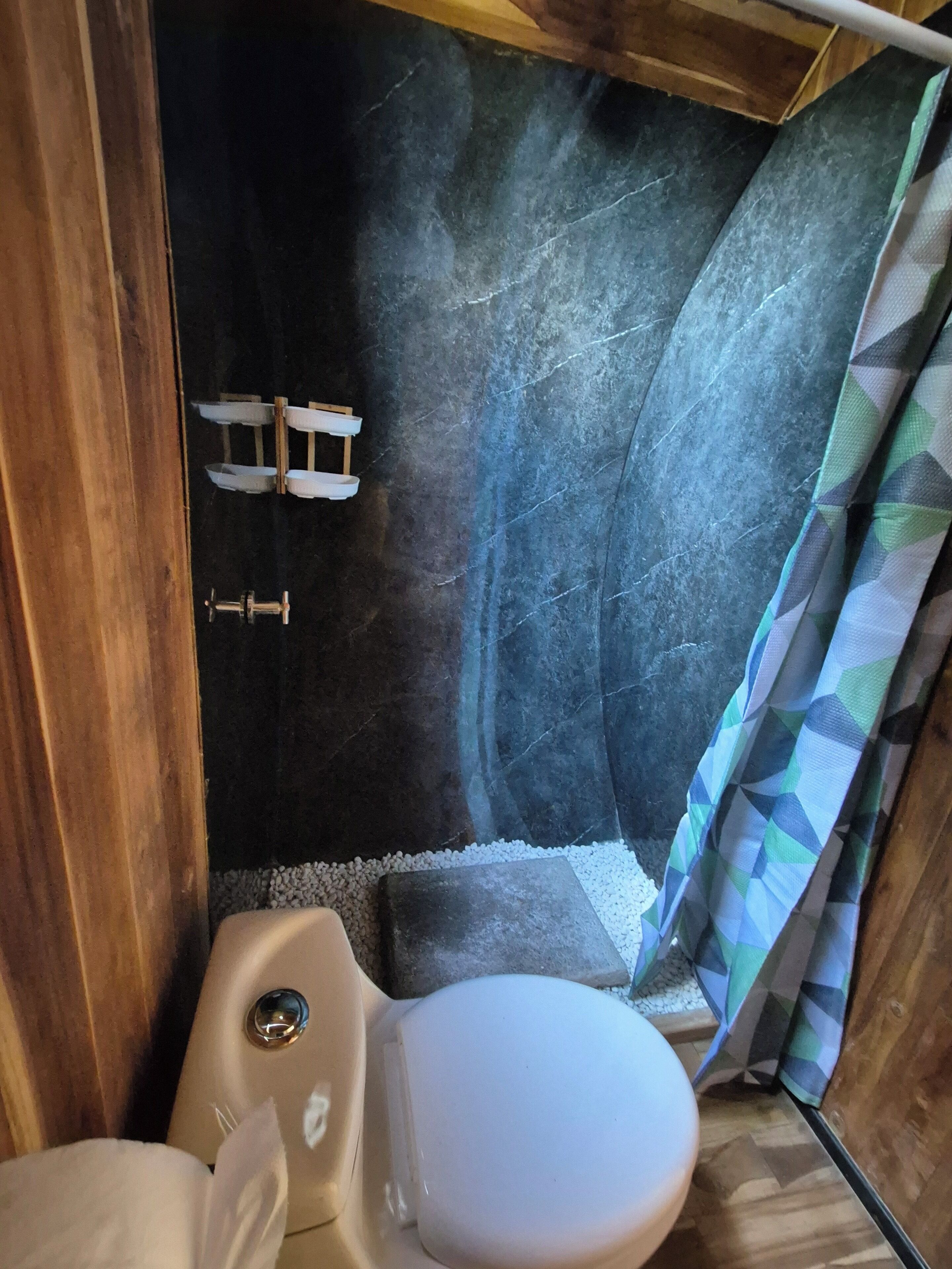 A compact bathroom with a toilet, a shower area, and a small shelf.
