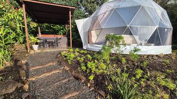 Une structure en forme de dôme géodésique dotée d’un espace extérieur aménagé avec des sièges et d’un sentier traversant un jardin.