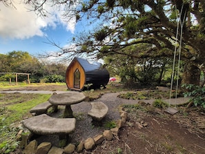 A wooden cabin with a circular entrance, surrounded by a garden with stone seating and a swing. - Glampling Nubes de Monteverde (Monteverde)