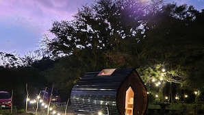 A small, wooden, barrel-shaped structure with a skylight, surrounded by string lights and set in a natural landscape. - Glampling Nubes de Monteverde (Monteverde)