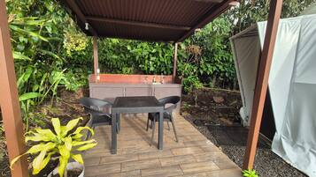 An outdoor patio with a covered seating area, a built-in sink, and surrounding greenery.